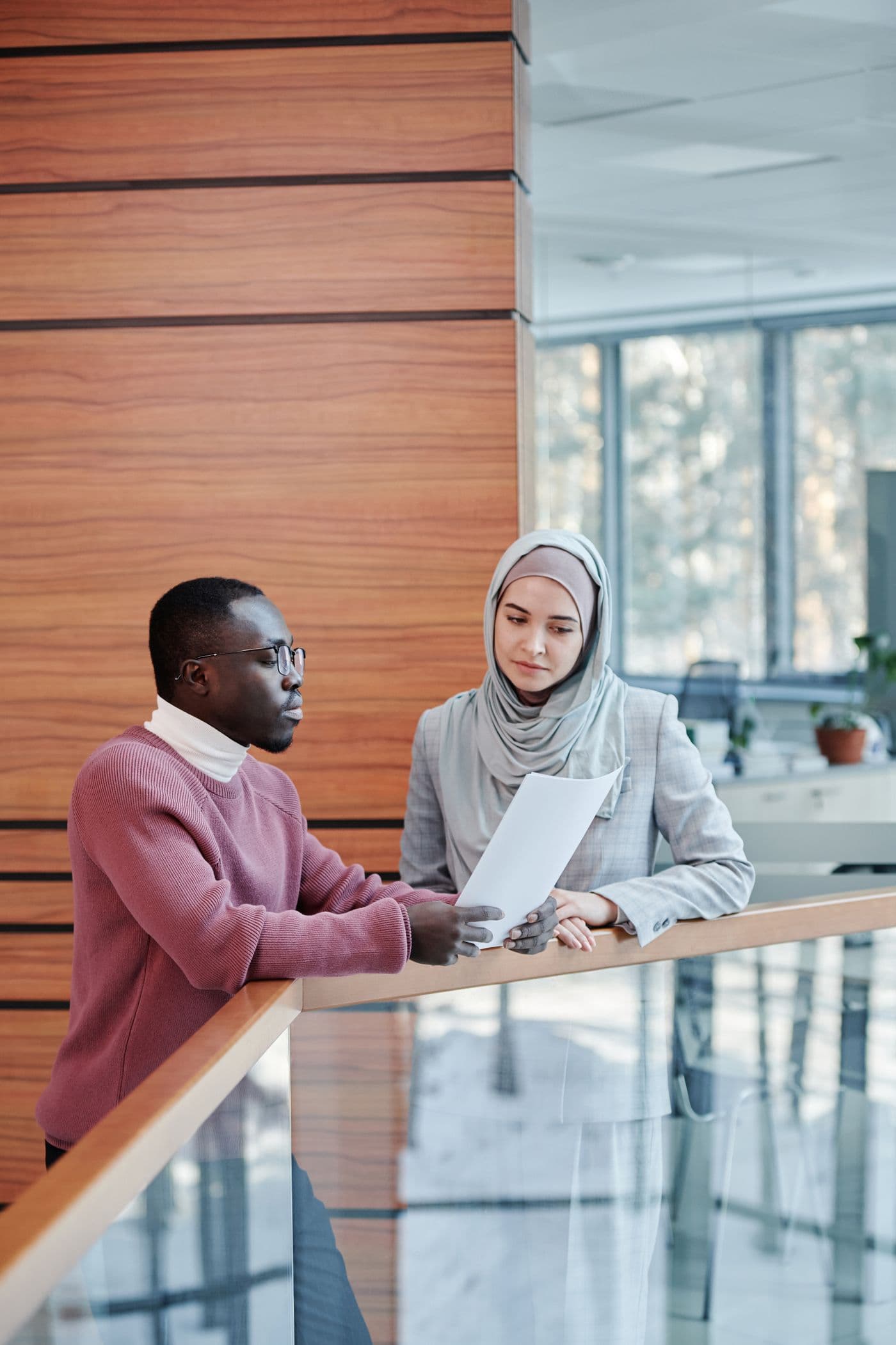 Two colleagues talking over a document beside a window in a light, timber-lined room